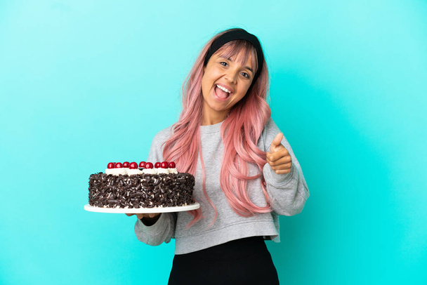 Mladá žena s růžovými vlasy drží narozeninový dort izolované na modrém pozadí s palci nahoru, protože se stalo něco dobrého - Fotografie, Obrázek