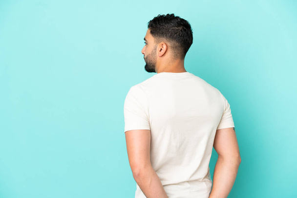 Young arab man isolated on blue background in back position and looking back - Foto, Bild