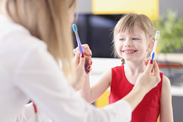 Dentist doctor offering little girl two toothbrushes to choose from in clinic - Foto, Imagem