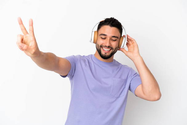 Genç Arap adam beyaz arka planda izole edilmiş müzik dinliyor ve şarkı söylüyor. - Fotoğraf, Görsel