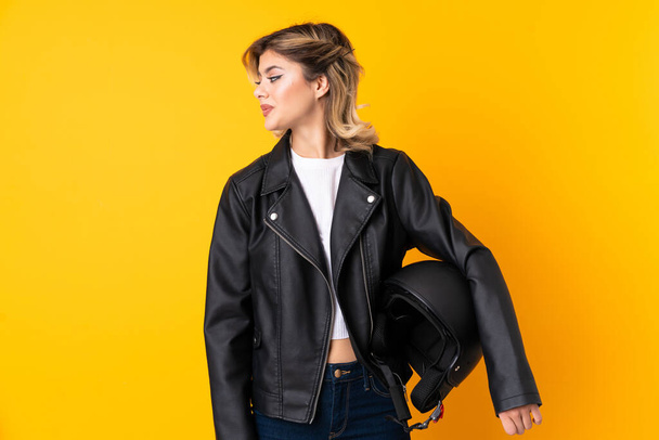 Teenager woman holding a motorcycle helmet isolated on yellow background looking to the side - Photo, Image