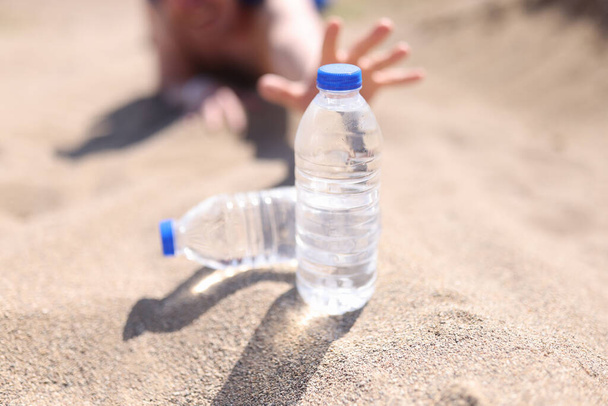 Manos masculinas que alcanzan para botella de agua de plástico en primer plano desierto - Foto, Imagen