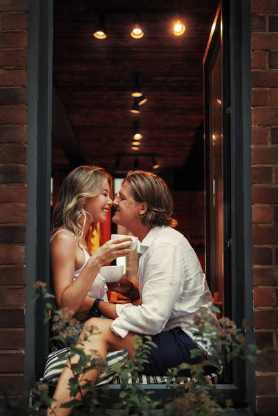 Happy Romantic Couple laughing and drinking coffee or tea in window of coffee shop. Beautiful Man and style woman are merry on date. Love expression - Fotoğraf, Görsel