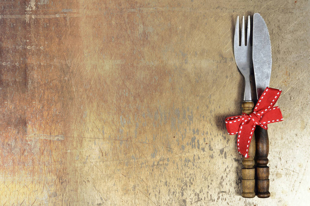 Vintage fork and knife tied with red ribbon on rusty grunge background with copy space - Photo, Image