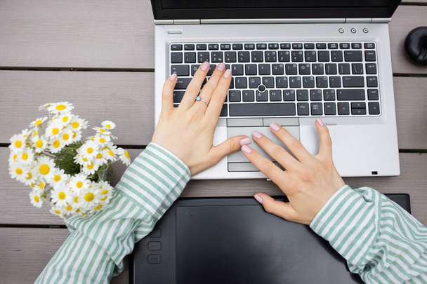 gray laptop keyboard, black graphic tablet, a bouquet of daisies and female hands in a striped shirt. office, business woman, designer, student, modern digital technologies, online communication - Photo, Image