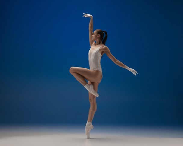 Young beautiful ballerina in action isolated over blue background. Concept of beauty, art, show, theater. - Фото, зображення