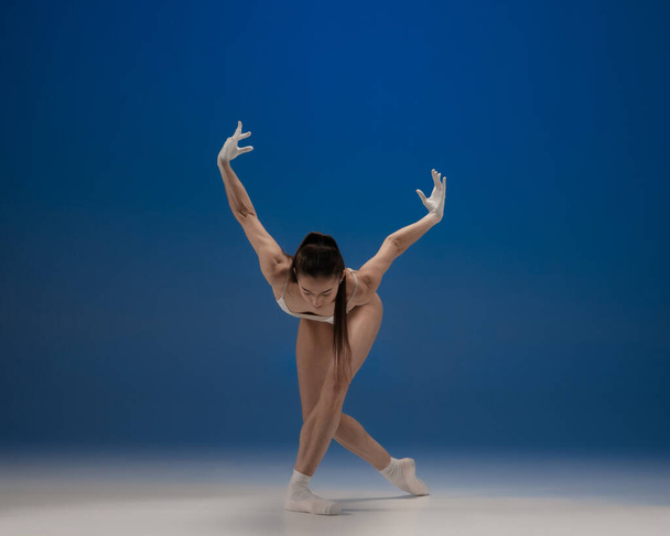 Junge schöne Ballerina in Aktion isoliert über blauem Hintergrund. Konzept von Schönheit, Kunst, Show, Theater. - Foto, Bild