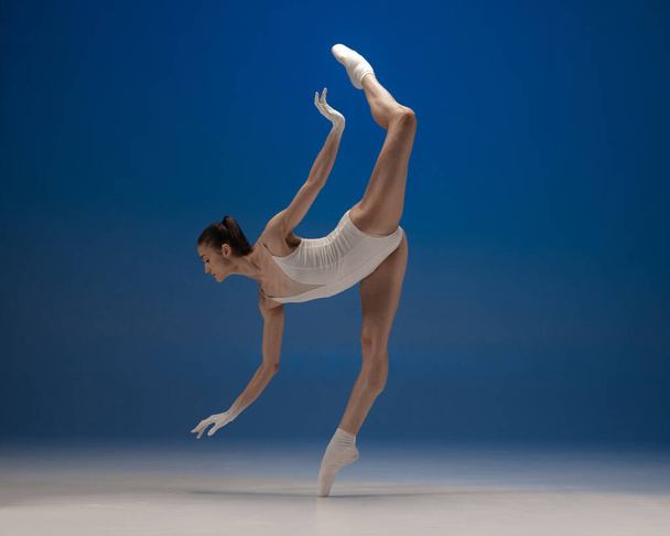 Λεπτή τρυφερή νεαρή όμορφη κοπέλα, χορεύτρια μπαλέτου που χορεύει απομονωμένη σε μπλε φόντο. - Φωτογραφία, εικόνα