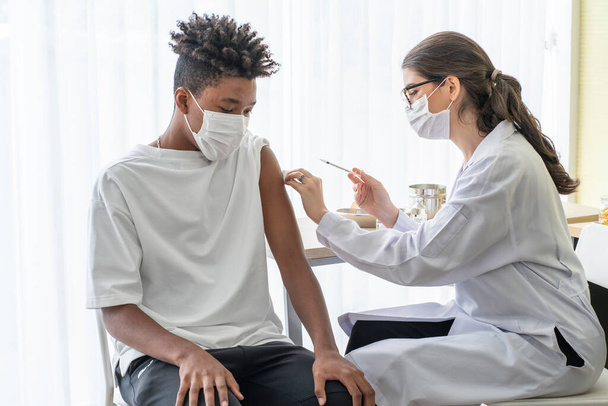 Médica usando um saco de mão, um frasco de vacina e uma seringa para evitar a propagação de COVID-19 Vacinar um homem afro-americano em uma estação vacinal.  - Foto, Imagem