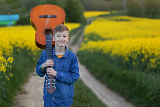 Portrait handsome boy with guitar walking on the summer road. Young musician on the road to success. - 写真・画像