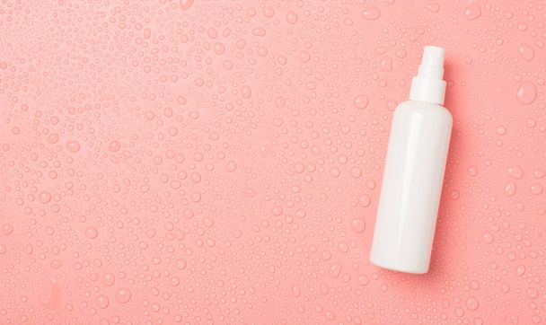 Top view photo of spray bottle without label on the right and water drops on isolated pink background with copyspace on the left - Photo, Image
