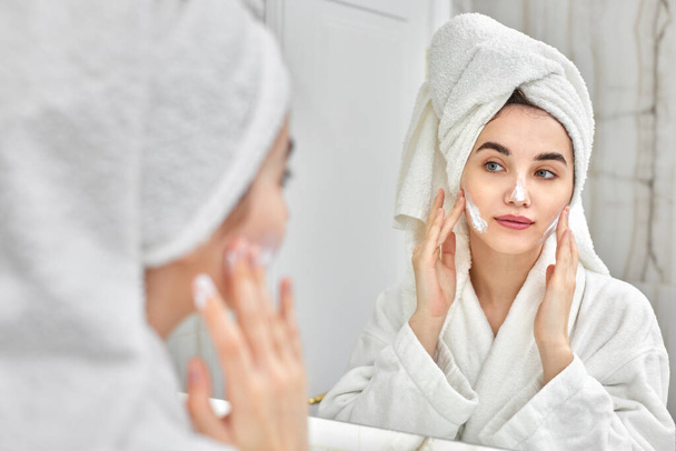 woman in white bathrobes applying apply facial cream - Foto, Bild