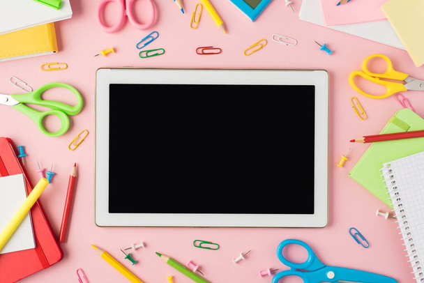 Top view fotó többszínű írószer ceruza ceruzák klipek számológép emlékeztető olló és tabletta számítógép kijelző közepén elszigetelt pasztell rózsaszín háttér copyspace - Fotó, kép