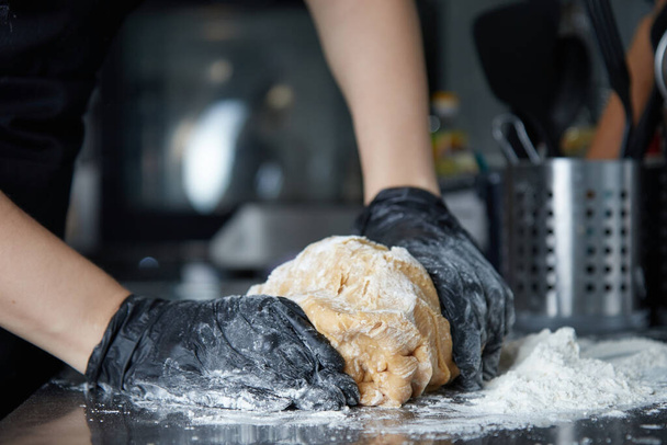 cook with gloved hands kneads dough on the table side view - Foto, Imagen