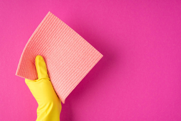 Top view photo of hand in yellow glove holding pastel pink rag on isolated pink background with blank space - Photo, Image