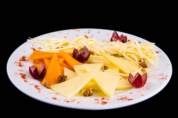 Assiette au fromage - Charcuterie Plateau avec différents types de fromage à pâte dure et fromage à ficelle., décoré de raisins, sur plaque blanche isolée sur fond noir vue de dessus - Photo, image