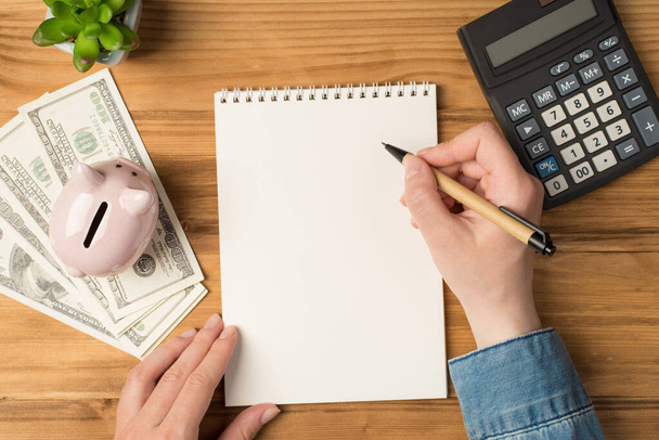 Above photo of notebook pen hands money earnings cash green plant moneybox and calculator isolated on the wooden backdrop - Photo, Image