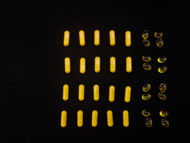 Żółte kapsułki są rozmieszczone na czarnym tle w formie harmonogramu przyjmowania na miesiąc - Zdjęcie, obraz