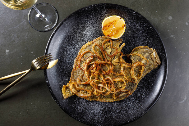 fried flounder with onion and lemon on a black clay plate - Photo, Image