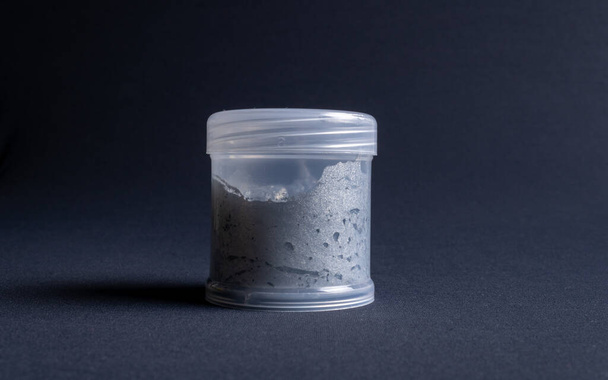 A pot containing resin of a white glitter color on a dark black background. Used for various purposes in industry and at home in the adaptation of furniture and objects for interior decoration. - Foto, Imagen