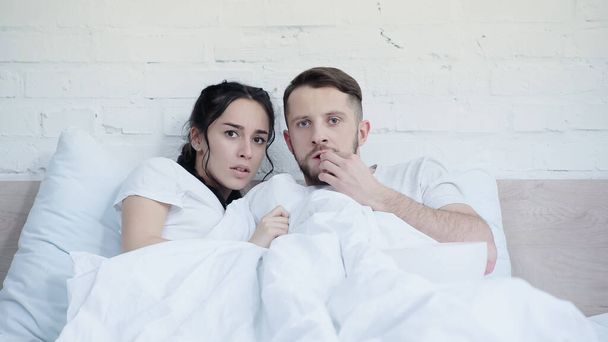 worried woman watching scary movie with boyfriend near popcorn in bedroom  - Fotografie, Obrázek