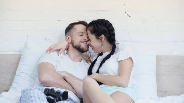 KYIV, UKRAINE - 2021年6月17日:ベッドの上でジョイスティックの近くに若い陽気な女性の抱擁男 - 写真・画像
