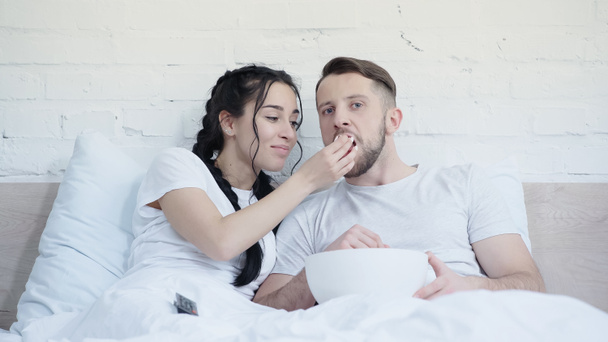 счастливая молодая пара ест попкорн и смотрит кино в постели - Фото, изображение