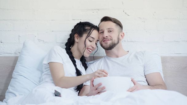 happy young couple with popcorn smiling and watching movie in bed - Photo, Image