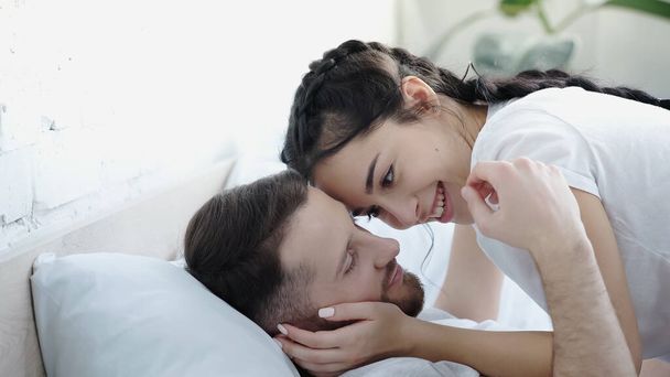 szczęśliwa młoda kobieta dotykając twarz brodatego mężczyzny w sypialni  - Zdjęcie, obraz