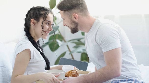 happy man bringing breakfast to smiling girlfriend with braids in bed - Photo, Image
