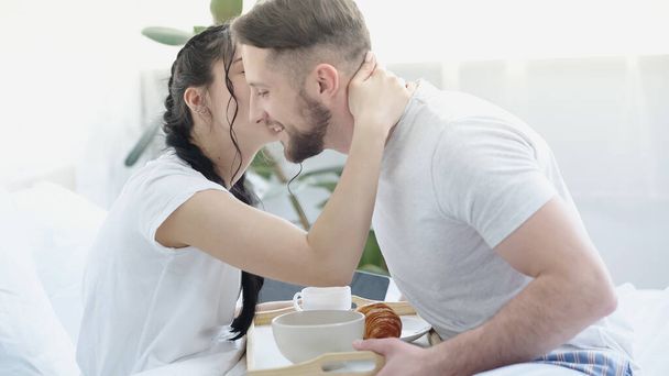 woman with braids kissing bearded man bringing breakfast in bed - Photo, image