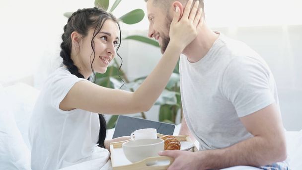 bearded man bringing breakfast to pretty girlfriend with braids in bed - Photo, Image