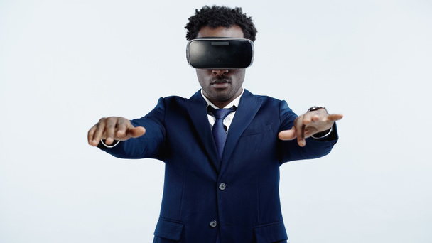 encaracolado empresário afro-americano de terno e fone de ouvido vr em pé com as mãos estendidas isoladas no azul - Foto, Imagem