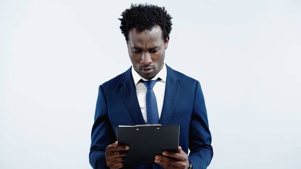 serious african american businessman looking at clipboard isolated on blue - Fotó, kép