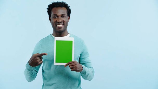 homem americano africano feliz apontando com o dedo para tablet digital com tela verde isolado em azul - Foto, Imagem