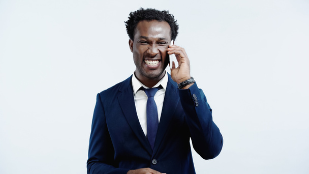 Χαρούμενος Αφροαμερικάνος επιχειρηματίας με κοστούμι που μιλάει στο κινητό του απομονωμένος στο μπλε - Φωτογραφία, εικόνα
