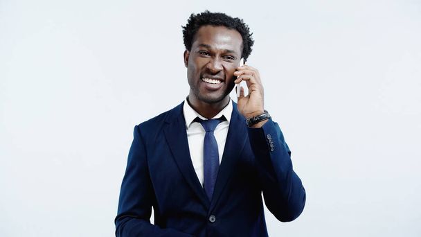 boldog afro-amerikai üzletember öltönyben beszél mobiltelefon elszigetelt kék - Fotó, kép