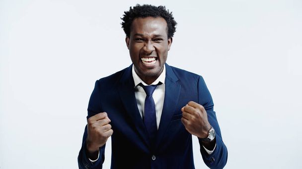 excited african american businessman with clenched fists isolated on blue - Foto, imagen