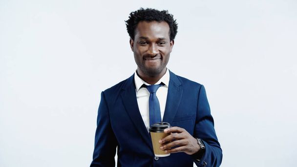 fröhliche afrikanisch-amerikanische Geschäftsmann hält Pappbecher isoliert auf blau - Foto, Bild