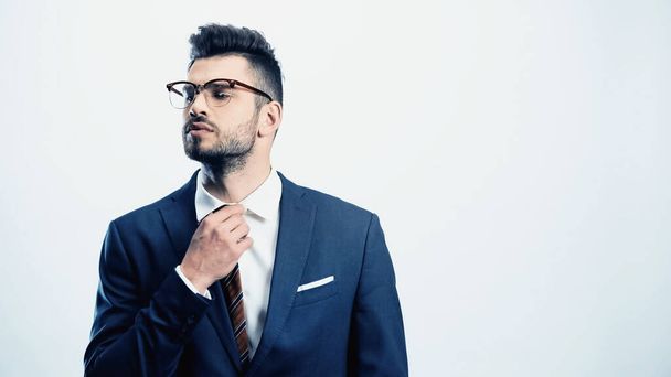 homem de negócios confiante em óculos ajustando gravata isolada no branco - Foto, Imagem