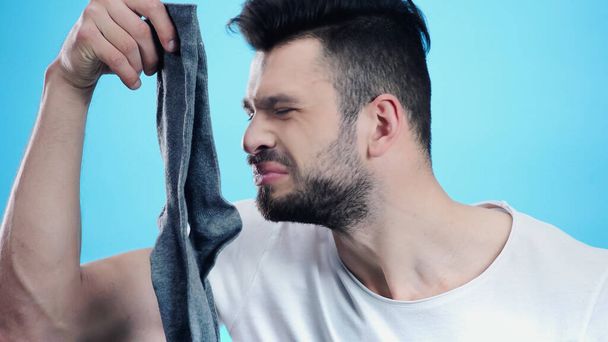 grimacing man smelling stinky sock isolated on blue - Foto, immagini