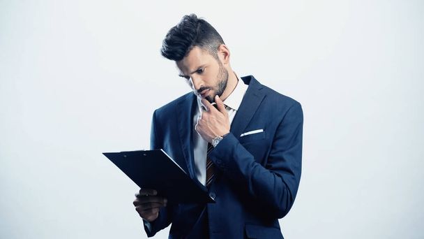 thoughtful businessman holding hand near face while looking at clipboard isolated on white - Φωτογραφία, εικόνα