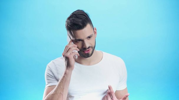 discouraged man pointing at himself with finger while talking on smartphone isolated on blue - Photo, Image
