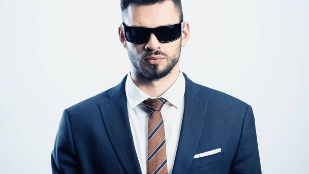 joven hombre de negocios en traje y gafas de sol oscuras mirando a la cámara aislada en blanco - Foto, imagen