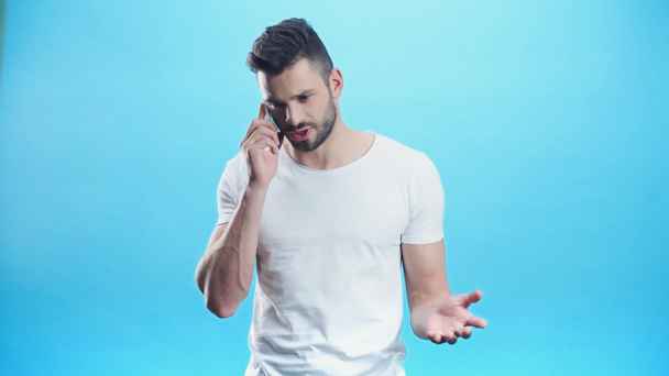 upset man gesturing during conversation on cellphone isolated on blue - Foto, immagini