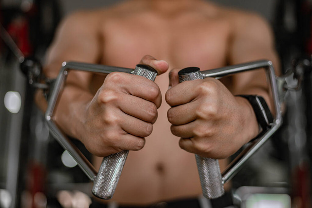 Concepto de gimnasio de entrenamiento un adolescente masculino musculoso usando un equipo de gimnasio que repite empujando hacia adelante para desarrollar su pecho. - Foto, imagen