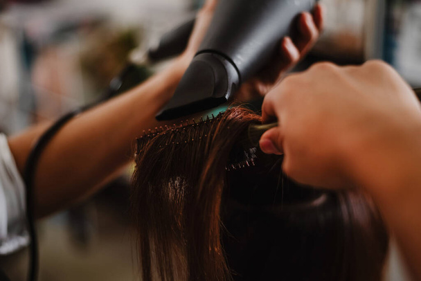 Friseursalon-Konzept: Ein männlicher Friseur greift mit einem Kamm nach einer Haarlocke und benutzt einen Haartrockner zum Trocknen und Glätten - Foto, Bild