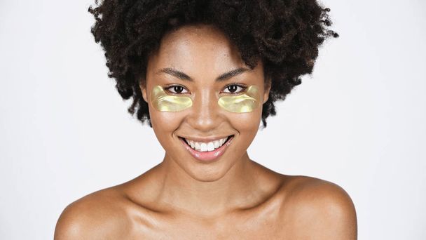 Uśmiechnięta Afroamerykanka ze złotymi przepaskami na oku odizolowana na szaro  - Zdjęcie, obraz