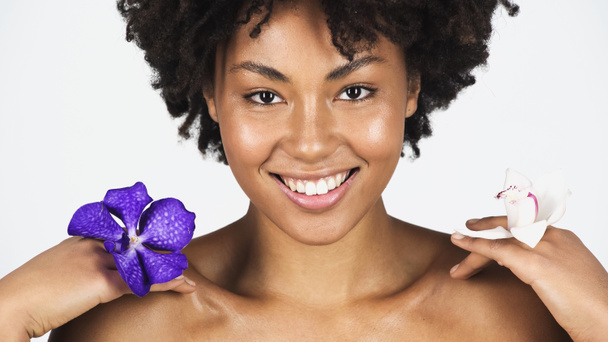 Досить африканська американка посміхається, тримаючи квіти орхідей ізольовані на сірому  - Фото, зображення