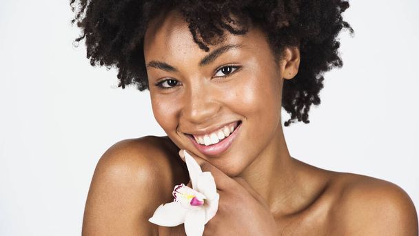 Pretty african american woman with clean skin holding orchid isolated on grey  - Фото, изображение